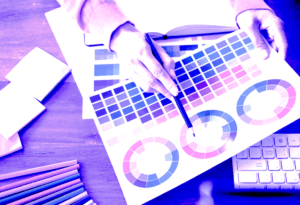 Designer selecting colors from a palette and color wheel during brand design planning on a wooden workspace
